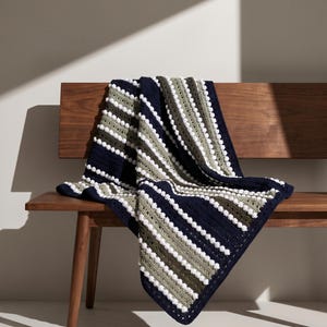 Könnte beinhalten: Eine gehäkelte Decke mit horizontalen Streifen in Marineblau, Salbeigrün und Weiß. Das Design enthält Reihen kleiner weißer Noppenstiche zwischen den farbigen Streifen. Der Text BOLD STRIPED THROW und Instant PDF Pattern • Confident Beginner ist zu sehen.