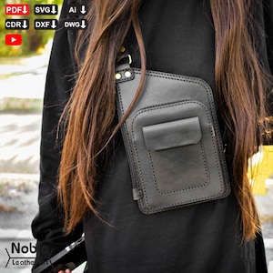 Puede incluir: Bolso bandolera de cuero negro con bolsillo delantero y cierre de cremallera. El bolso tiene un diseño cosido y se lleva al hombro. El bolso es de Noble Leather Art.