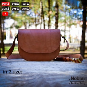 May include: A brown leather saddlebag with a curved flap and adjustable strap. The bag has a brass buckle and is displayed on a wooden surface. The text "in 2 sizes" is visible. The bag is from Noble Leather Art.