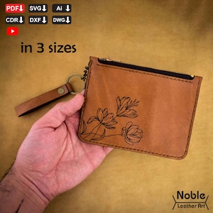 May include: A tan leather wallet with a black zip and a wrist strap. The wallet has a floral design and the text "in 3 sizes". The Noble Leather Art logo is in the bottom right corner.