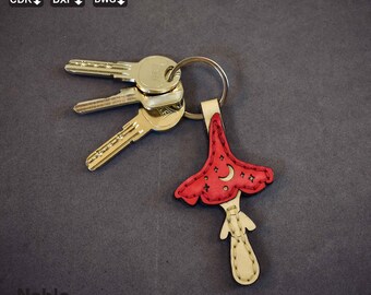 Peut inclure: Un porte-clés en cuir rouge et crème en forme de champignon avec un croissant de lune et des étoiles. Le porte-clés est attaché à un anneau argenté avec trois clés. Le texte "Noble Leather Art" est également présent.