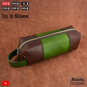 May include: A rectangular leather pencil case with a green center panel and brown end panels. The case has a gold zipper and a small green handle. The text "In 3 Sizes" is visible.