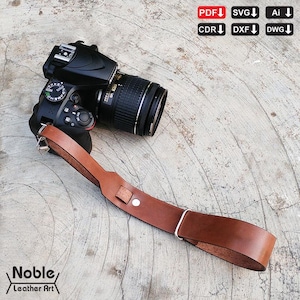 May include: A black DSLR camera with a brown leather strap. The strap is attached to the camera with silver metal hardware. The words "Noble Leather Art" are printed on the bottom left corner of the image.