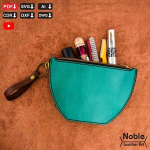 Può includere: Un astuccio in pelle turchese con cerniera dorata e cinturino da polso in pelle marrone. L'astuccio contiene vari cosmetici. Il testo "Noble Leather Art" si trova in basso a destra.