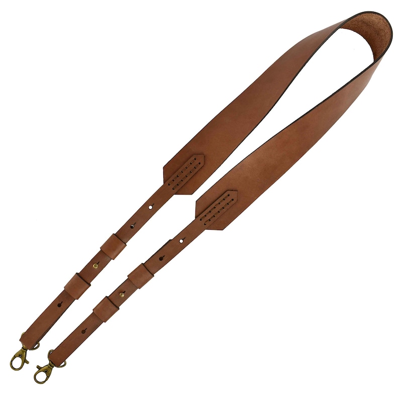K&ouml;nnte beinhalten: Ein brauner Leder-Schulterriemen mit messingfarbenen Drehverschl&uuml;ssen. Der Riemen hat verstellbare Abschnitte und ist f&uuml;r die Verwendung mit einer Tasche oder einem anderen Gegenstand konzipiert. Das Leder scheint von hoher Qualit&auml;t zu sein und hat eine nat&uuml;rliche Maserung.