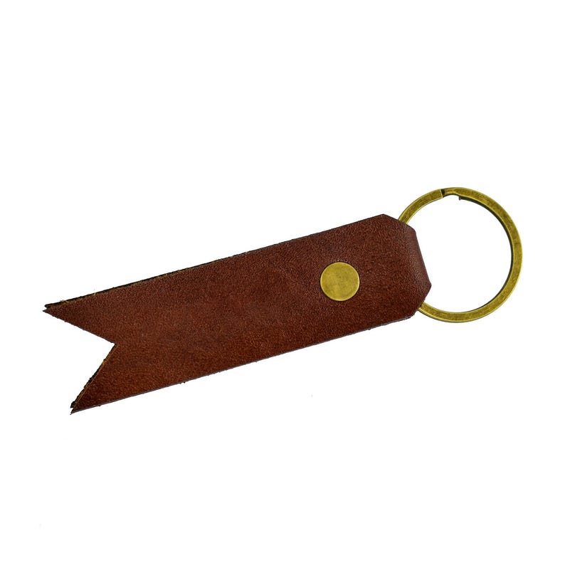 May include: A brown leather keychain with a brass-colored key ring and a gold-colored rivet. The keychain has a pointed end and is set against a white background.