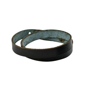 May include: A dark brown leather wrap bracelet with a brass button closure. The bracelet is wrapped around itself, showing the light blue interior of the leather. The bracelet is designed to be worn around the wrist.