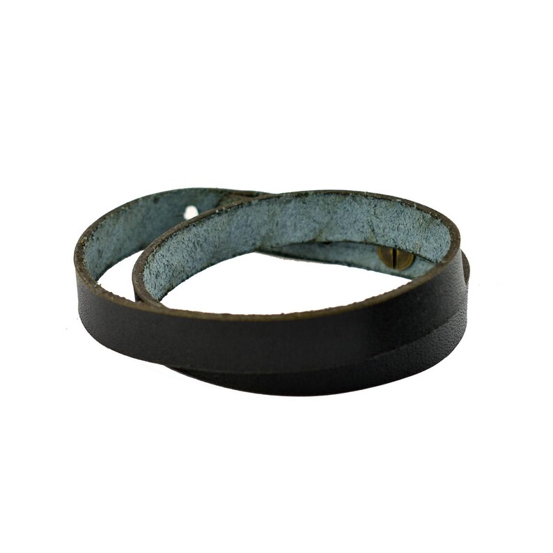 May include: A dark brown leather wrap bracelet with a brass button closure. The bracelet is wrapped around itself, showing the light blue interior of the leather. The bracelet is designed to be worn around the wrist.