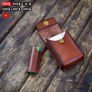 Könnte beinhalten: Ein braunes Lederkartenetui und Feuerzeug-Etui-Set. Das Kartenetui ist geöffnet und zeigt eine weiße Karte. Das Feuerzeug-Etui ist zylindrisch mit Messingnieten. Beide Artikel liegen auf einer Holzoberfläche.