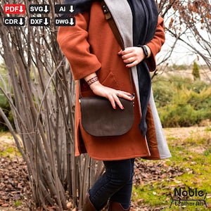 Peut inclure: Un sac à bandoulière en cuir marron foncé avec un rabat inférieur incurvé, porté sur un manteau couleur rouille. Le sac a une longue bandoulière réglable. L'image montre également une écharpe noire, un bracelet en cuir et le texte "Noble Leather Art".