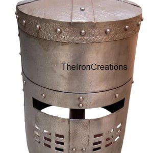 以下が含まれることがあります： 丸みを帯びた上部とリベットのディテールが施された、銀色の中世のヘルメット。 ヘルメットは、長方形の目と口の開口部を備えた円筒形のボディをしています。 テキスト「ThelronCreations」が側面に印刷されています。