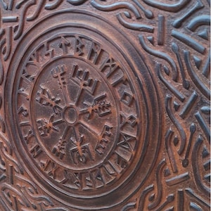May include: A round, brown, wooden shield with intricate carved Viking knotwork and a central compass design. The shield features a weathered, rustic appearance, with the text "TheIronCreations" at the bottom.