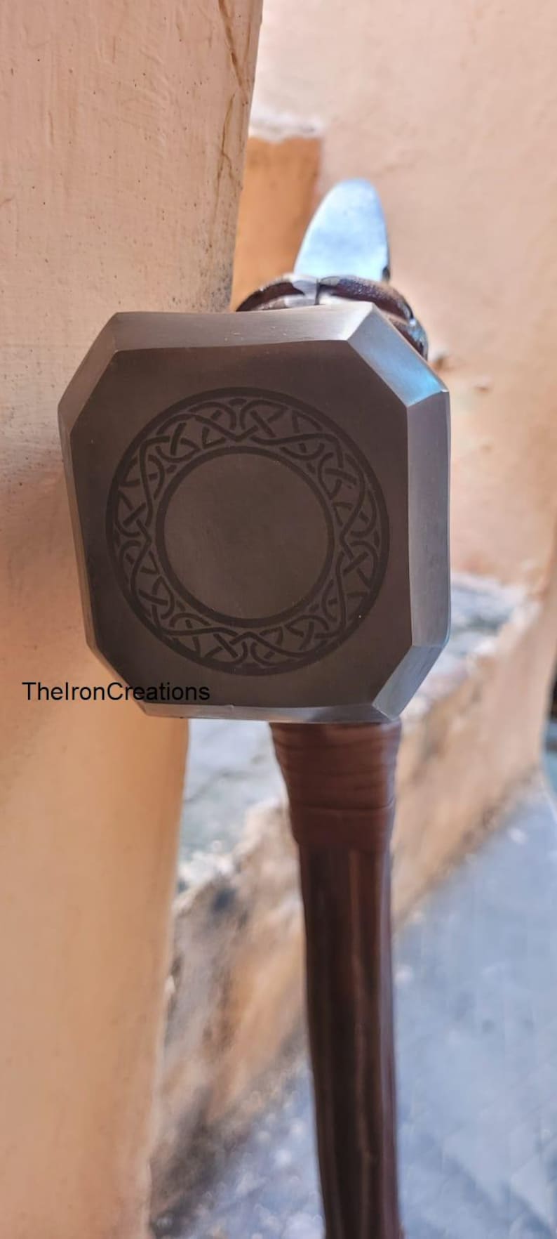 May include: A dark gray metal hammer with a geometric design on the head and a brown handle. The text "ThelronCreations" is visible on the side of the hammer.