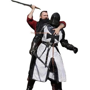 May include: A person in a red shirt and black scarf holds a sword above a person wearing a black and white medieval knight's armor. The armor features a black cross on the chest and a black helmet.