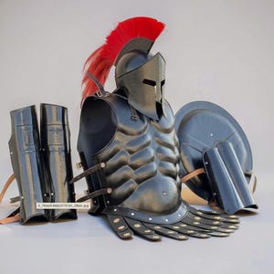 May include: A black metal suit of armor featuring a Corinthian-style helmet with a vibrant red crest, a muscular breastplate with leather straps, a set of greaves, and a round shield. The armor includes decorative gold-toned circular accents.