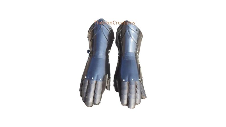 May include: Pair of black metal gauntlets. The gauntlets are made of overlapping metal plates and are designed to protect the hands and wrists. The gauntlets have a dark, reflective finish and are likely part of a suit of armor.