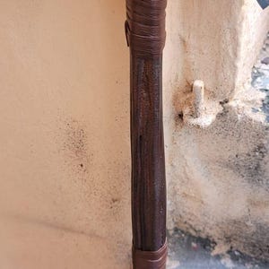 May include: Close-up of a prop axe with a dark brown wooden handle wrapped in brown leather. The axe head is gray. The text "ThelronCreations" is visible on the side.