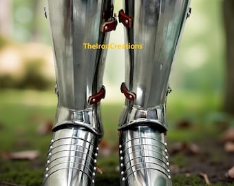 May include: A pair of polished steel greaves and sabatons featuring articulated metal plates covering the feet and lower legs. The armor includes brown leather straps with metal buckles for fastening. The text TheIronCreations is visible.