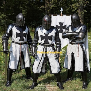 May include: Three figures in medieval knight armor stand in a grassy area. The armor is black and silver, with white tunics featuring large black crosses. Each knight wears a helmet and carries a sword or has crossed arms. A banner with a black cross is in the background.