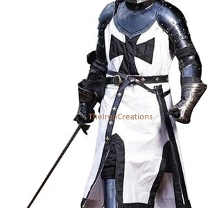 May include: A full suit of medieval knight armor, including a helmet, chest plate, and leg protection. The white tunic features a large black cross. The armor is detailed with metal accents and a black belt. A sword is held in the right hand.