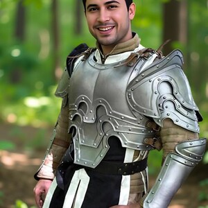 May include: A silver-colored medieval armor set with intricate detailing, including a breastplate, shoulder guards, and arm protection. The armor is worn over a brown and black garment. The image is set in a forest.