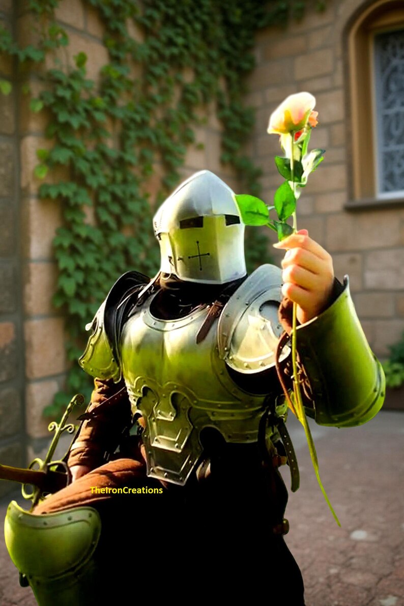 May include: A person in medieval armor, holding a rose. The armor is a metallic green color with a silver helmet featuring a cross. The rose has a yellow and pink bloom. The background includes a brick wall and greenery.