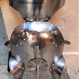 May include: A polished steel breastplate with a flared neck guard and shoulder defenses. The armor features rivets and a central decorative element. The text "ThelronCreations" is visible on the neck guard.