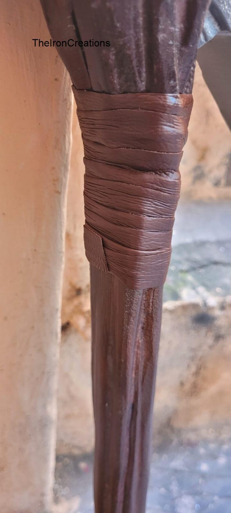 May include: Close-up of a dark brown wooden object with a wrapped leather detail. The leather is a lighter shade of brown and is wrapped around the wooden object. The text "TheIronCreations" is visible.