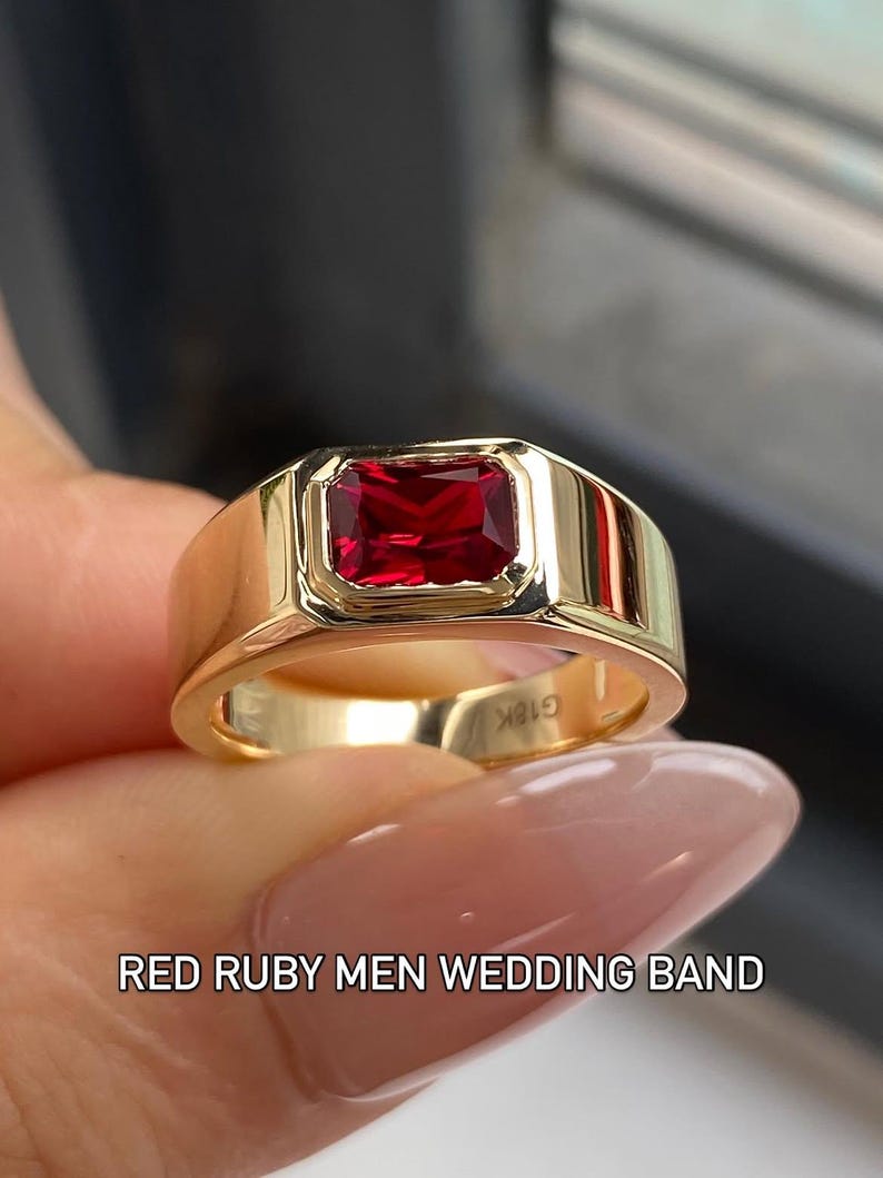 K&ouml;nnte beinhalten: Ein goldener Ring mit einem rechteckigen roten Rubin in einer Zargenfassung. Das Band hat eine polierte Oberfl&auml;che und die Innenseite ist mit dem Text G18K graviert. Der Text RED RUBY MEN WEDDING BAND ist unten im Bild zu sehen.