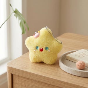 May include: A plush yellow star-shaped keychain with a small pink crown and decorative blue and red accents. The star has a silver chain and is decorated with small pearls. A cute and whimsical accessory.