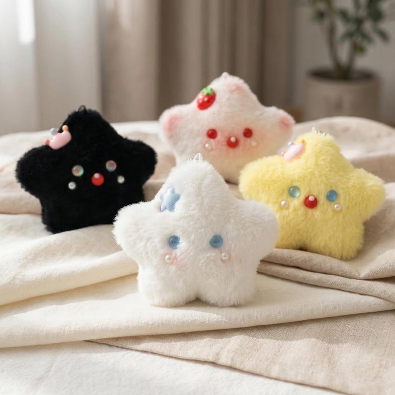 May include: A collection of five plush star-shaped keychains in various colors. The keychains are black, white, pink, and yellow, with embroidered details including eyes, mouths, and decorative accents. Each star has a small metal loop for attachment.