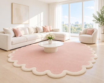 May include: A large, circular area rug featuring a solid light pink center and a thick, scalloped cream-colored border. The rug is positioned on a light-toned wooden floor, providing a soft, textured contrast to the surrounding furniture.