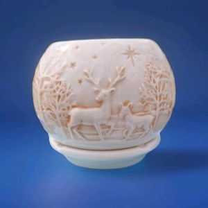May include: Cream-colored ceramic candle holder with a winter scene featuring deer, trees, and stars. The spherical holder sits on a matching saucer base. The embossed design adds a textured, dimensional quality to the piece.