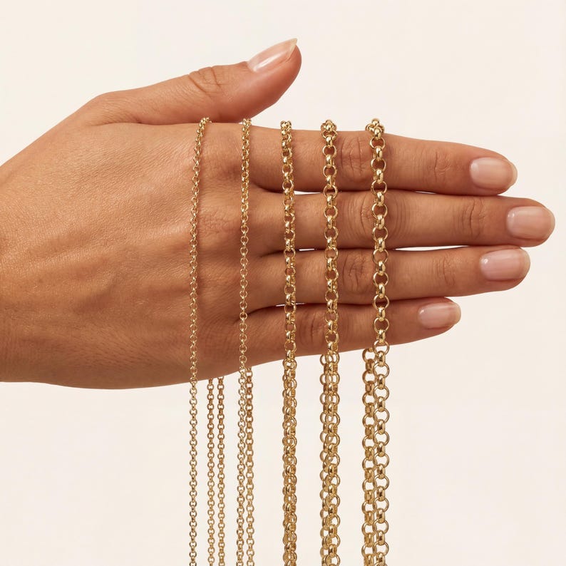 May include: A hand displays a selection of gold-colored chain necklaces. The chains vary in thickness, with delicate and thicker options. The necklaces are displayed against a neutral background, highlighting the jewelry's shine and detail.
