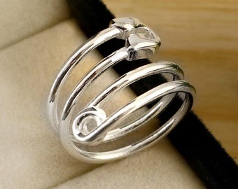 May include: A silver-colored ring with a unique, layered design. The ring features three curved bands that wrap around the finger, with a floral-shaped accent at the top. The ring is displayed in a dark blue jewelry box.