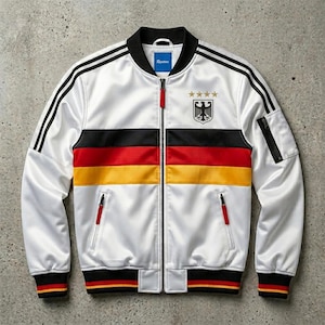 May include: A white bomber jacket featuring black, red, and yellow horizontal stripes across the chest. The jacket has a black collar, cuffs, and hem with red and yellow accents. A German eagle emblem with four gold stars sits on the left chest.