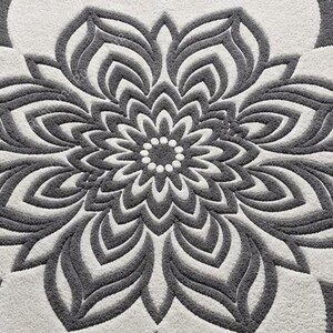 May include: A tufted rug featuring a large, symmetrical floral mandala pattern in dark gray and off-white. The design consists of concentric layers of petal shapes radiating from a central circle of small dots, with a textured, plush surface.