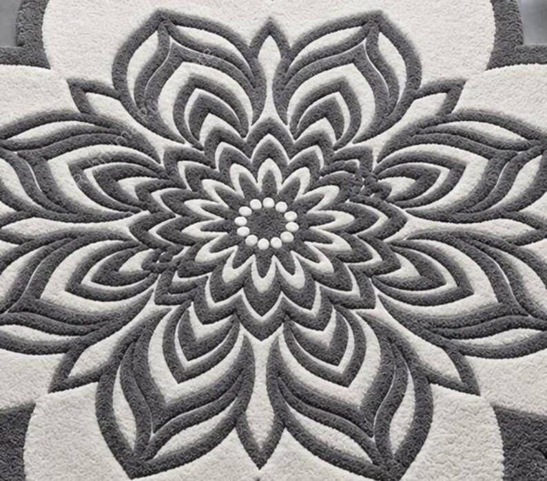 May include: A tufted rug featuring a large, symmetrical floral mandala pattern in dark gray and off-white. The design consists of concentric layers of petal shapes radiating from a central circle of small dots, with a textured, plush surface.