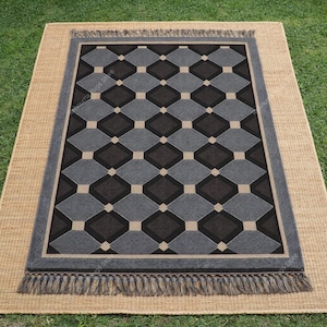 May include: Rectangular rug with a geometric diamond pattern in shades of gray and black, bordered by a gray frame and beige fringe. The rug is placed on a larger beige woven mat, set on green grass.