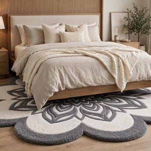 May include: A large, circular, flower-shaped area rug featuring a central mandala pattern in shades of dark gray and cream. The rug has a thick, textured pile with scalloped edges that extend outward, creating a distinct floral silhouette on the floor.
