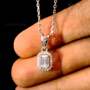 May include: A silver necklace with a rectangular pendant featuring a central, clear gemstone surrounded by smaller, clear stones. The chain is delicate, and the pendant is set against a dark background. The text "GOLD FLUSH" is visible.
