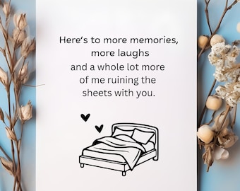 Può includere: Una carta bianca con il testo "Here's to more memories, more laughs and a whole lot more of me ruining the sheets with you." Un'illustrazione in bianco e nero di un letto con due cuori è sotto il testo. La carta è su uno sfondo blu con accenti floreali.