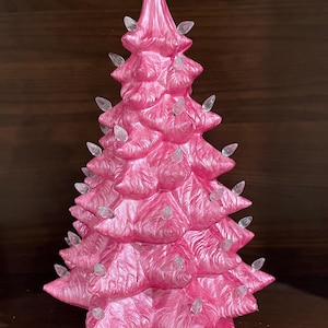 以下が含まれることがあります： 透明なライトが付いたピンク色のセラミッククリスマスツリー。木は質感のある表面とクラシックなデザインです。ライトは木全体に均等に配置されています。木のベースはスカラップのデザインです。
