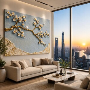 May include: A large rectangular wall art piece featuring a textured light blue background with a raised gold branch adorned with white cherry blossoms and a small white bird perched on the branch, with gold textured accents along the bottom edge.