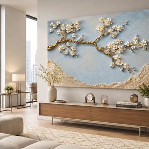 May include: A large rectangular wall art piece featuring a textured light blue background with a raised gold tree branch adorned with white flowers and a small white bird. The bottom section of the artwork displays a textured gold landscape element.