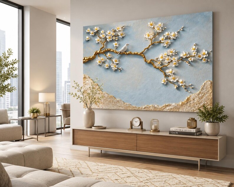 May include: A large rectangular wall art piece featuring a textured light blue background with a raised gold tree branch adorned with white flowers and a small white bird. The bottom section of the artwork displays a textured gold landscape element.