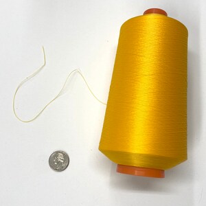 May include: A spool of bright yellow thread with a small amount of thread unwound. The spool is about the size of a US quarter.