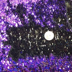 May include: Purple and black iridescent fabric with a textured, scaly pattern. The fabric is made of sequins and has a shimmery finish.