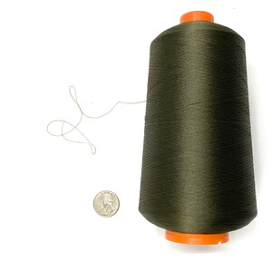 May include: A spool of dark green thread with an orange plastic bobbin.