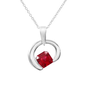 Könnte beinhalten: Eine silberne Anhängerkette mit einem leuchtenden, quadratisch geschliffenen roten Edelstein. Der Edelstein ist in einem wirbelnden, offenen Kreisdesign gefasst. Die Halskette hat eine feine Silberkette.